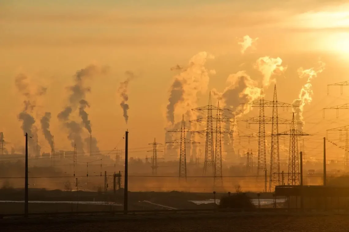 Electrical towers at golden hour with distant smoke rising, highlighting environmental impact and the need for environmentally conscious actions.