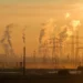 Electrical towers at golden hour with distant smoke rising, highlighting environmental impact and the need for environmentally conscious actions.