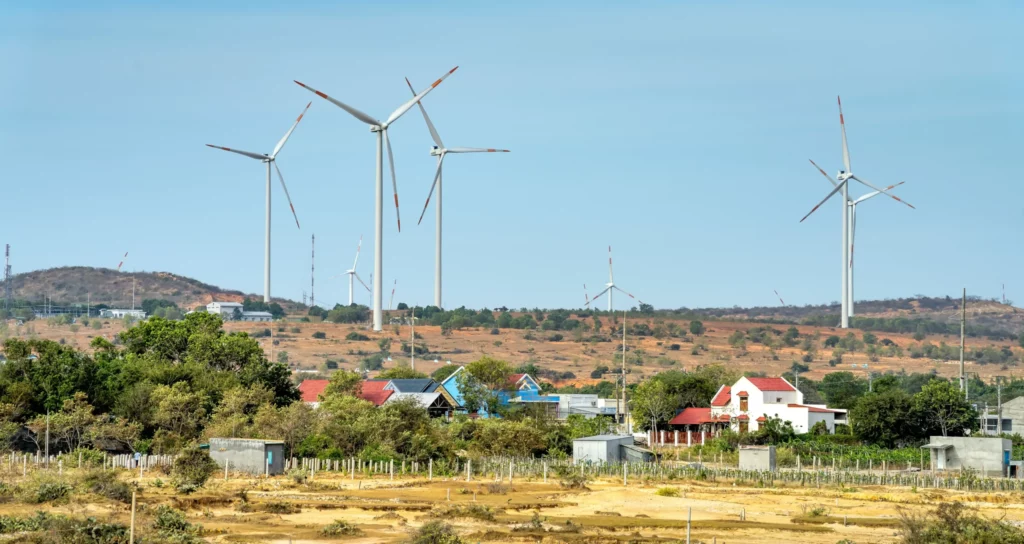 Wind turbines in a barren land area near houses, harnessing renewable energy.