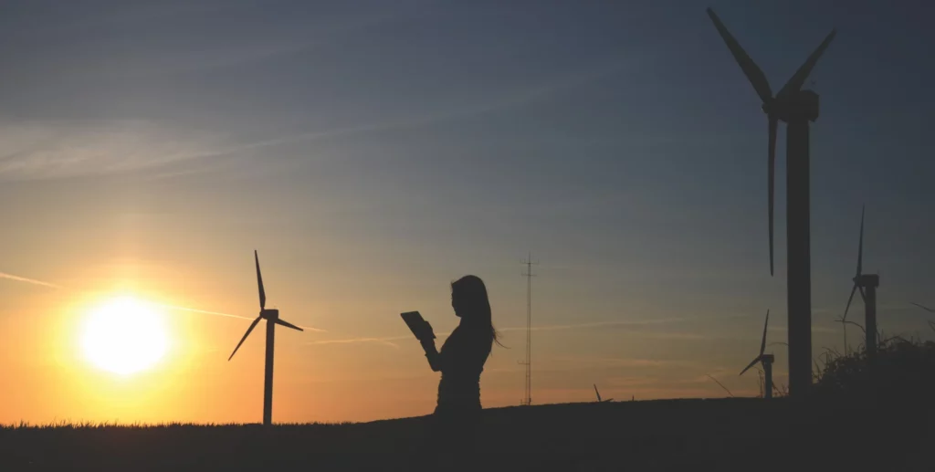 Woman using a tablet with wind turbines nearby, embracing a sustainable lifestyle.